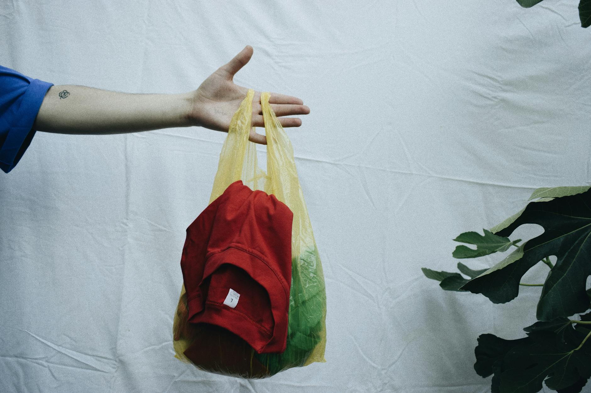 Dłoń trzyma żółtą torbę z używaną odzieżą na białym tle Dłoń trzyma żółtą torbę z używaną odzieżą na białym tle