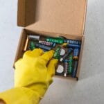 Ręka w żółtej rękawicy trzyma zużyte baterie przeznaczone do recyklingu