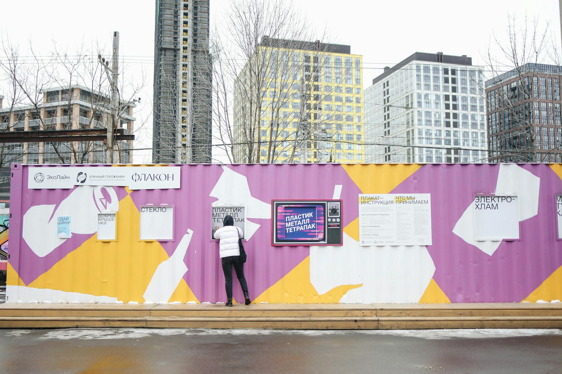 Osoba wrzuca odpady do kolorowych pojemników na miejskim punkcie recyklingu