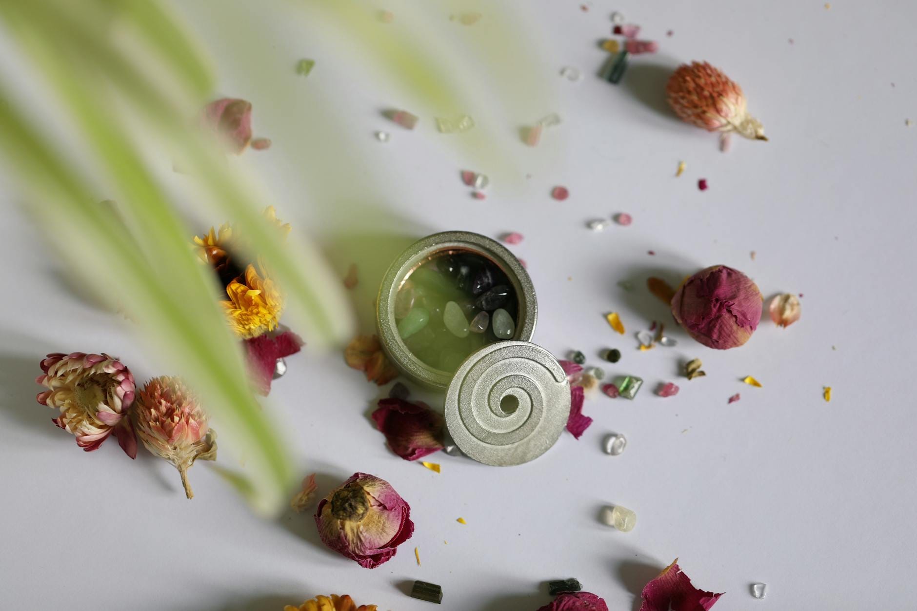 Ozdobna puszka wypełniona kamieniami wśród suszonych kwiatów na białym tle