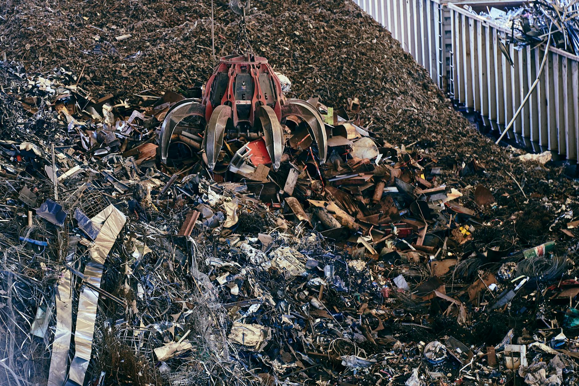 Koparka chwytakowa przerzuca dużą stertę złomu na złomowisku